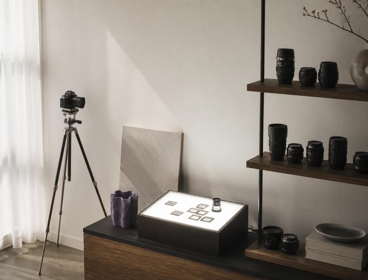 A calm studio corner with a tripod, lightbox and camera lenses